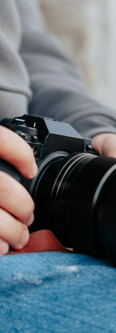 Eine Hand hält eine Kamera, während sie auf einer blauen Jeans sitzt.